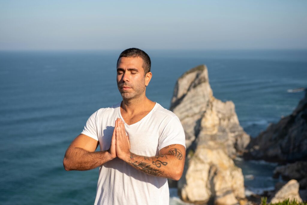 Man practicing meditation by the sea with a rocky backdrop in Portugal, capturing serenity and focus.